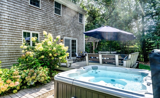 Hot tub on the deck surrounded by blooming hydrangeas, with the house and shaded pergola behind