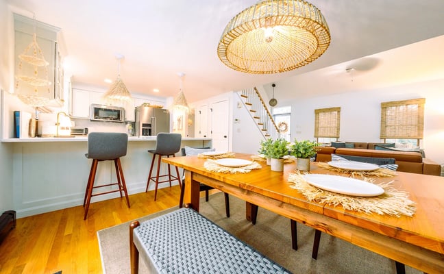 Open-plan kitchen and dining area with wooden table, bar seating, woven pendant lights, and staircase to upper level